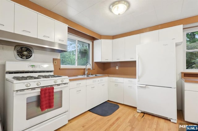 kitchen with white appliances, a sink, healthy amount of natural light, and white cabinets