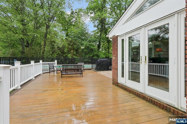 wooden deck with french doors, fence, a swimming pool, and view of scattered trees