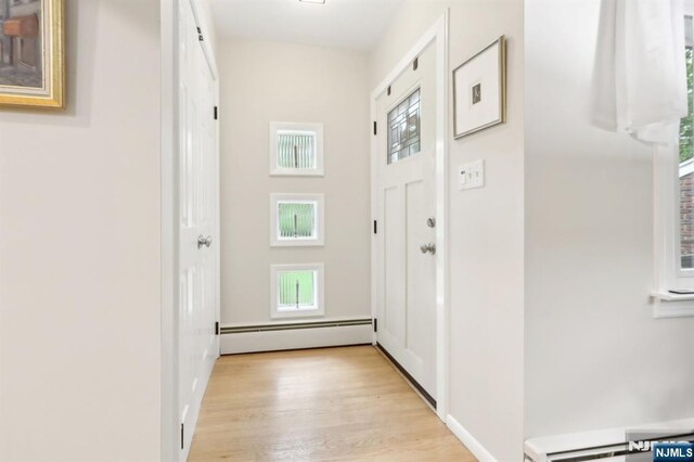 corridor with a baseboard heating unit, healthy amount of natural light, and light wood finished floors