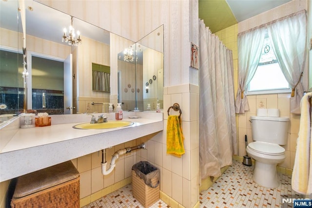 full bathroom featuring tile walls, a chandelier, a sink, toilet, and tile patterned flooring