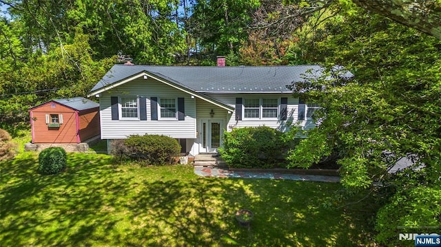split foyer home with a front yard, a chimney, and an outdoor structure