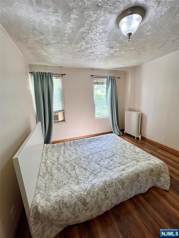 bedroom featuring radiator, wood finished floors, cooling unit, ornamental molding, and baseboards