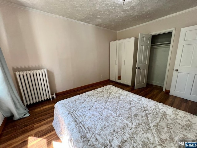 bedroom featuring radiator heating unit, dark wood finished floors, baseboards, two closets, and a textured ceiling