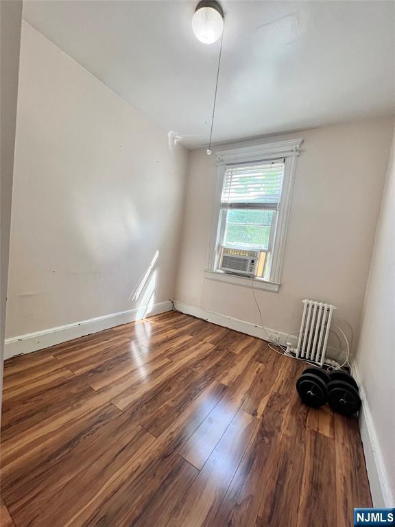 unfurnished room featuring wood finished floors, baseboards, cooling unit, and radiator heating unit