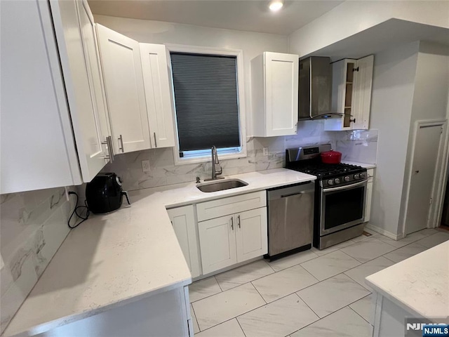 kitchen featuring appliances with stainless steel finishes, a sink, wall chimney exhaust hood, and backsplash