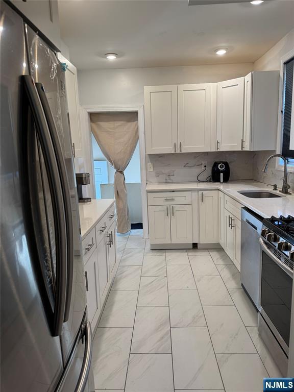 kitchen with appliances with stainless steel finishes, a sink, light countertops, light marble finish floors, and white cabinets
