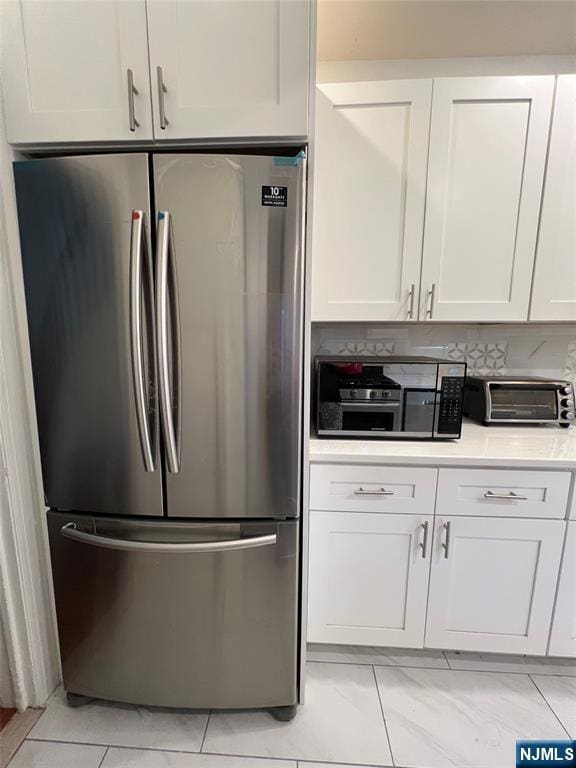 kitchen featuring stainless steel appliances, white cabinetry, light countertops, and light marble finish floors