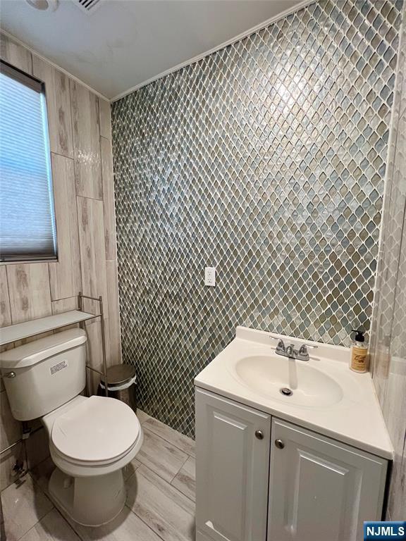 bathroom featuring tile walls, toilet, vanity, and ornamental molding