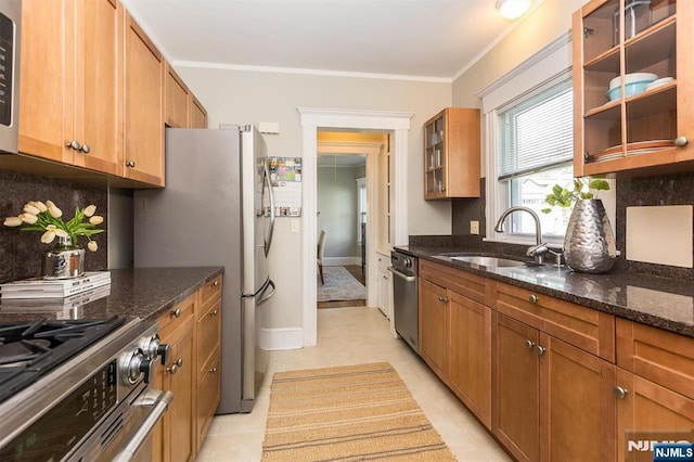 kitchen with a sink, dark stone counters, glass insert cabinets, light tile patterned floors, and ornamental molding