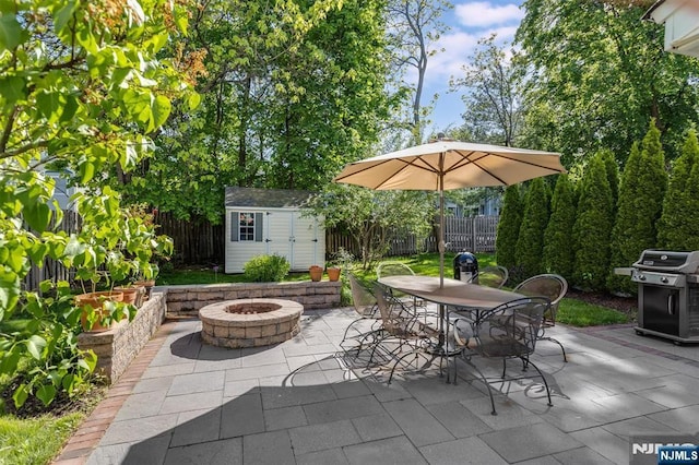 view of patio with a fire pit, a grill, a shed, an outbuilding, and fence