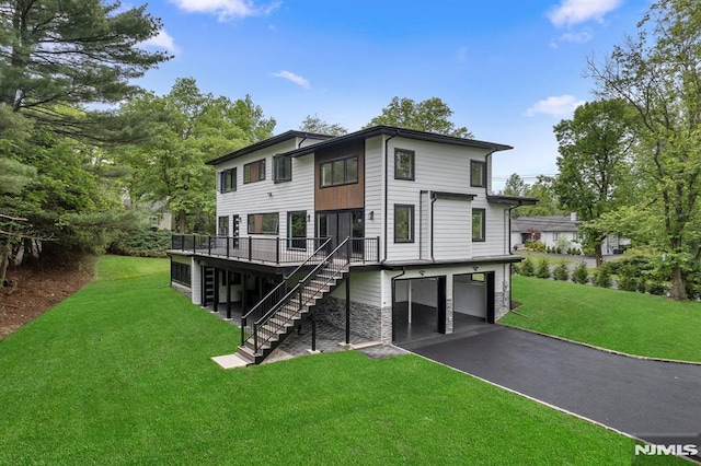 rear view of house with stairs, a garage, asphalt driveway, a wooden deck, and a lawn