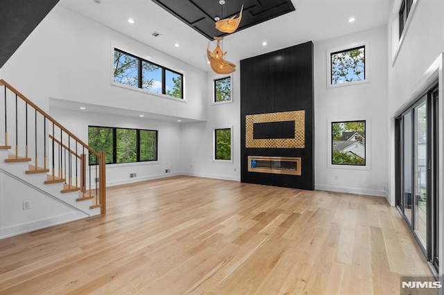 unfurnished living room featuring a towering ceiling, healthy amount of natural light, light wood-type flooring, a fireplace, and recessed lighting