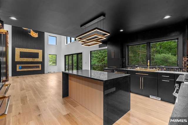 kitchen with dark cabinetry, open floor plan, a kitchen island, light wood finished floors, and recessed lighting