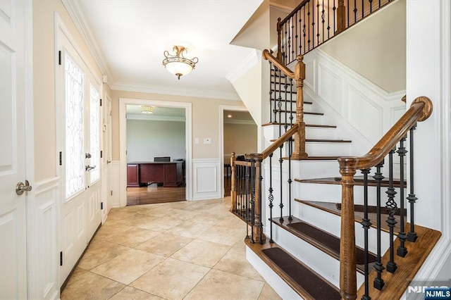 foyer entrance featuring a decorative wall, crown molding, a wainscoted wall, stairway, and light tile patterned floors