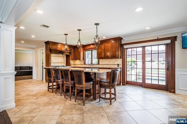 kitchen with ornate columns, ornamental molding, a sink, decorative backsplash, and pendant lighting