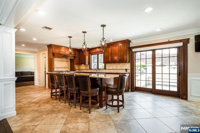 kitchen featuring ornate columns, a decorative wall, crown molding, a sink, and a kitchen breakfast bar