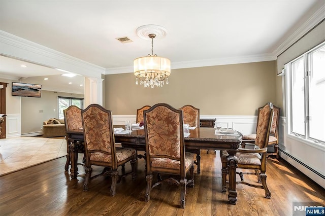 dining room featuring a baseboard heating unit, ornamental molding, a decorative wall, wainscoting, and a chandelier