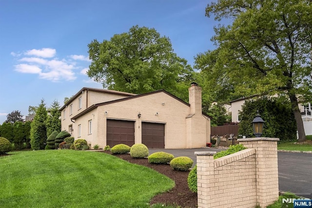 view of property exterior featuring a garage, asphalt driveway, a chimney, and a yard