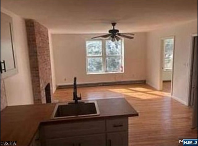 kitchen featuring a sink, ceiling fan, wood finished floors, baseboards, and dark countertops
