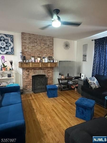 living area featuring ceiling fan, wood finished floors, and a brick fireplace