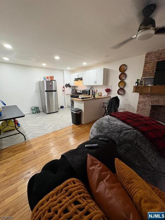 living area with parquet flooring, recessed lighting, a brick fireplace, and ceiling fan