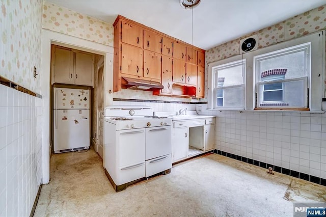 kitchen featuring white appliances, under cabinet range hood, wallpapered walls, tile walls, and light countertops