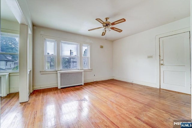 unfurnished living room featuring radiator, ceiling fan, light wood-style floors, and baseboards
