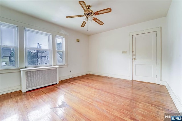 unfurnished room with radiator heating unit, light wood finished floors, baseboards, and a ceiling fan