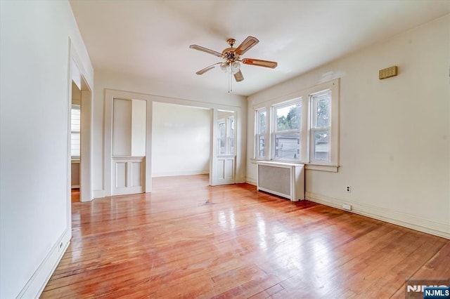 spare room featuring radiator heating unit, light wood-type flooring, a ceiling fan, and baseboards