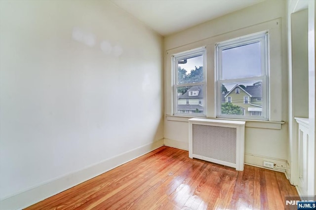 empty room with radiator heating unit, light wood finished floors, and baseboards