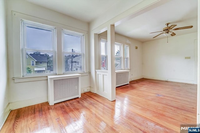 spare room with radiator, light wood-type flooring, ceiling fan, and baseboards