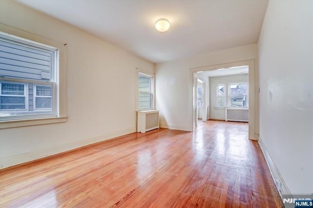 unfurnished room featuring wood finished floors, baseboards, and radiator heating unit