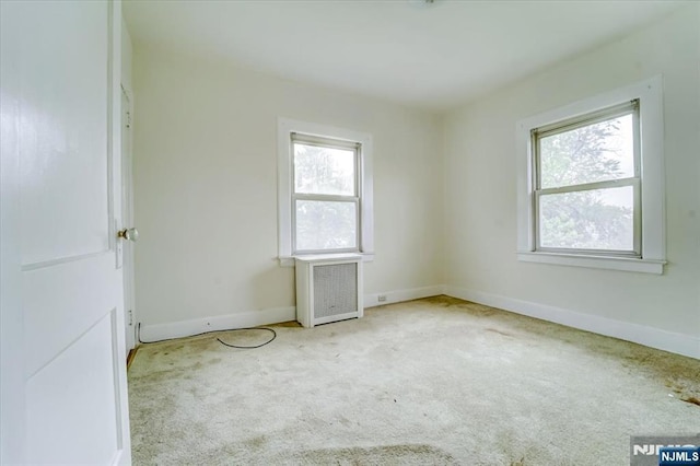 empty room with carpet flooring, radiator, and baseboards
