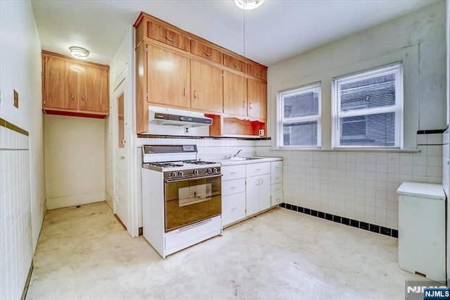 kitchen with white range with gas cooktop, under cabinet range hood, a sink, light countertops, and tile walls