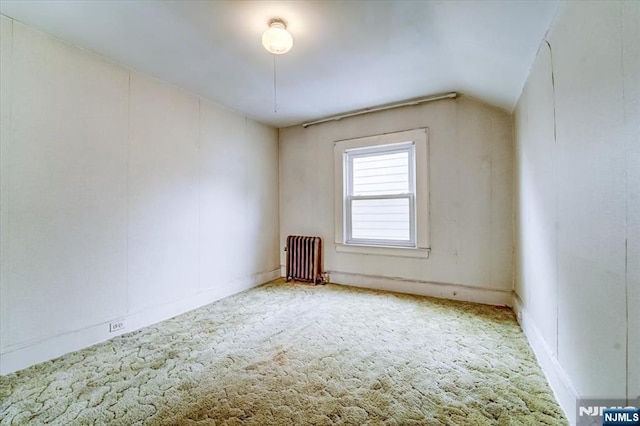 empty room with carpet floors, radiator, lofted ceiling, and baseboards