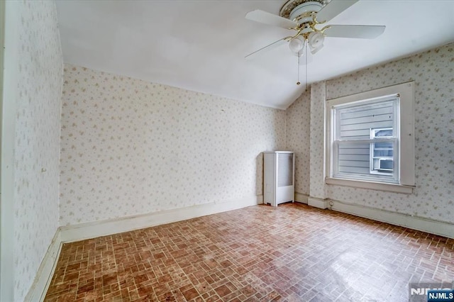 empty room featuring brick patterned floors, ceiling fan, wallpapered walls, vaulted ceiling, and baseboards