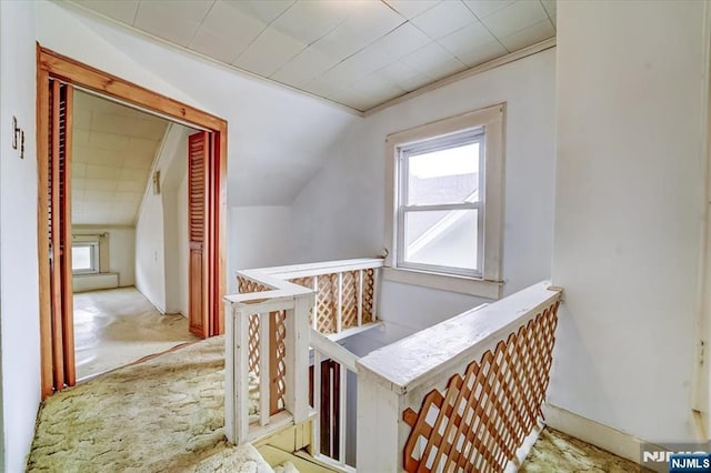 corridor featuring an upstairs landing, vaulted ceiling, and light colored carpet