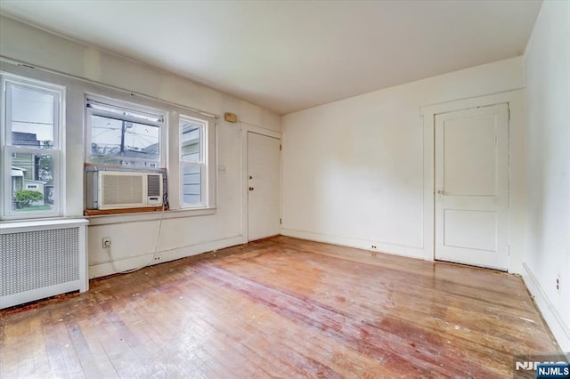 spare room featuring radiator heating unit, light wood-style flooring, cooling unit, and baseboards