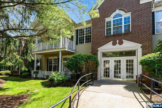 rear view of property with french doors, a balcony, brick siding, and a lawn