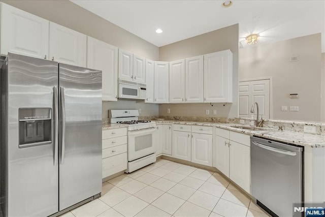 kitchen featuring stainless steel appliances, a sink, a peninsula, light stone countertops, and white cabinetry