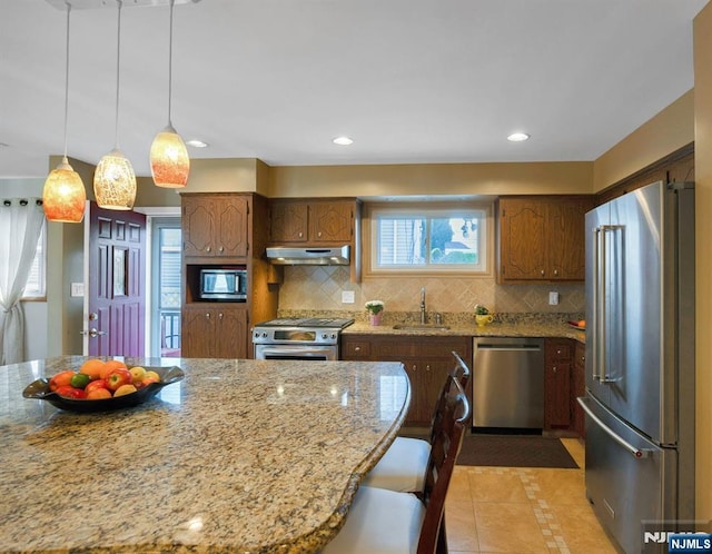kitchen featuring stainless steel appliances, under cabinet range hood, a sink, backsplash, and light tile patterned floors