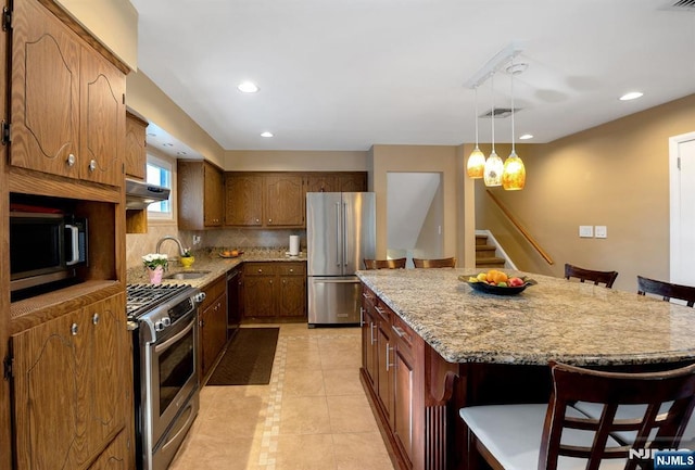 kitchen with appliances with stainless steel finishes, under cabinet range hood, a kitchen breakfast bar, decorative backsplash, and a kitchen island