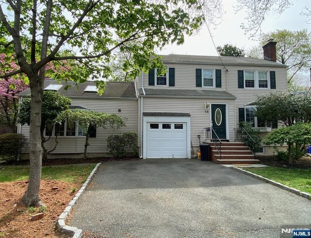 view of front facade with driveway, an attached garage, and a chimney