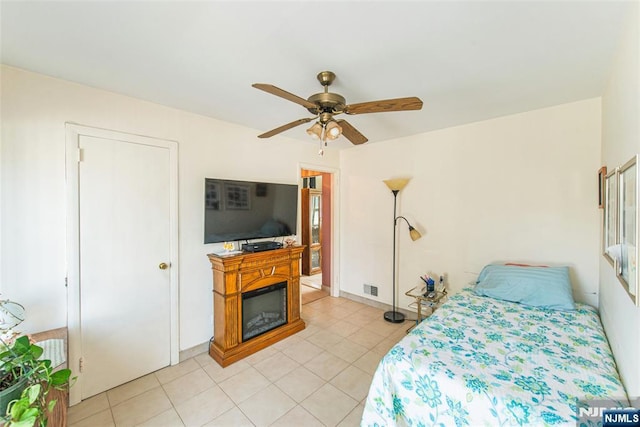 bedroom with light tile patterned floors, a glass covered fireplace, and ceiling fan