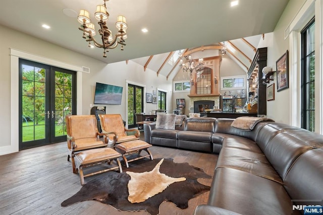 living area with a chandelier, french doors, wood finished floors, a warm lit fireplace, and recessed lighting