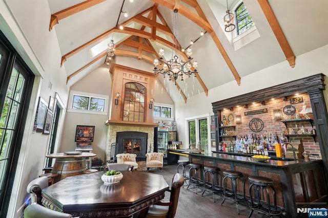 dining room with high vaulted ceiling, a bar, wood finished floors, beam ceiling, and a lit fireplace