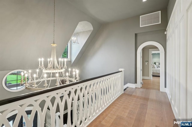 hallway featuring light wood finished floors, arched walkways, a chandelier, and baseboards