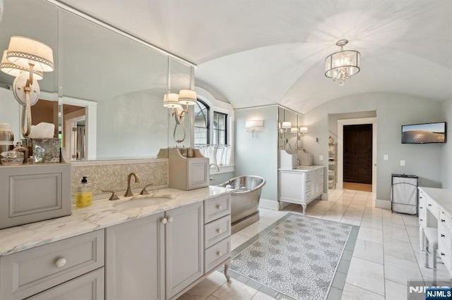 bathroom with vaulted ceiling, a chandelier, vanity, decorative backsplash, and a soaking tub