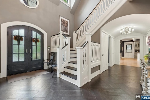 foyer entrance with arched walkways, french doors, stairway, baseboards, and a high ceiling