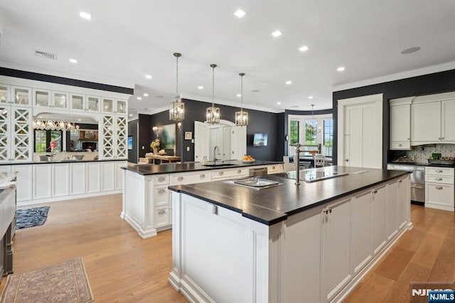 kitchen with a spacious island, dark countertops, a sink, ornamental molding, and white cabinets